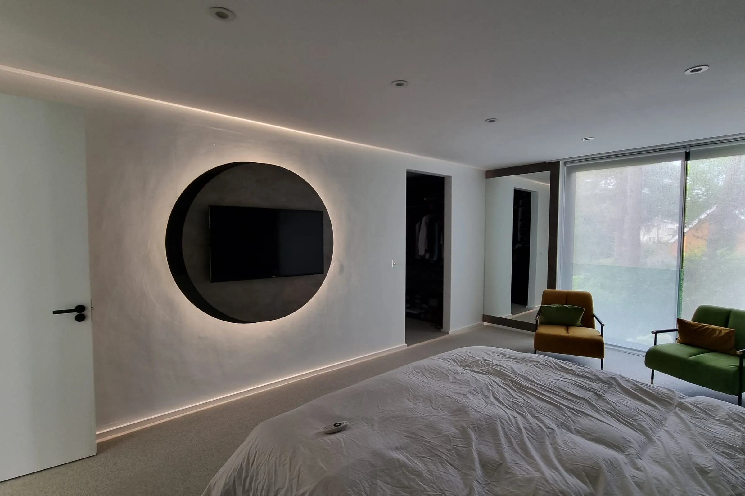 Fitted bedroom with a backlit circular TV feature on a plastered wall