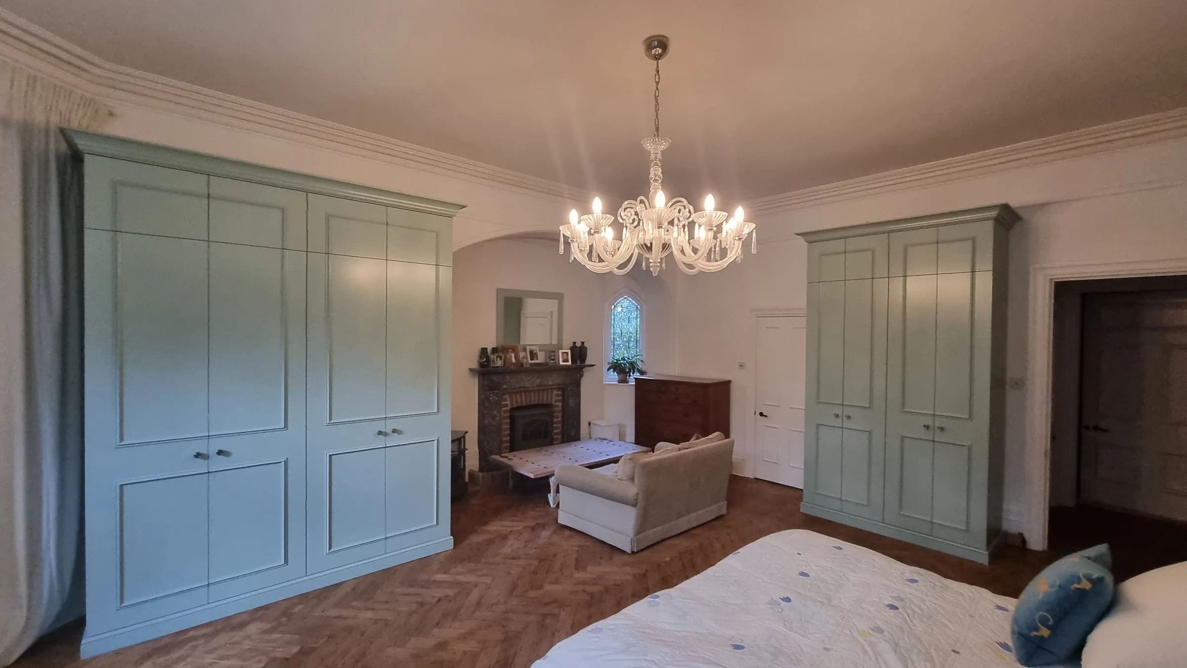 Two painted green fitted wardrobes either side of a fireplace in a period bedroom