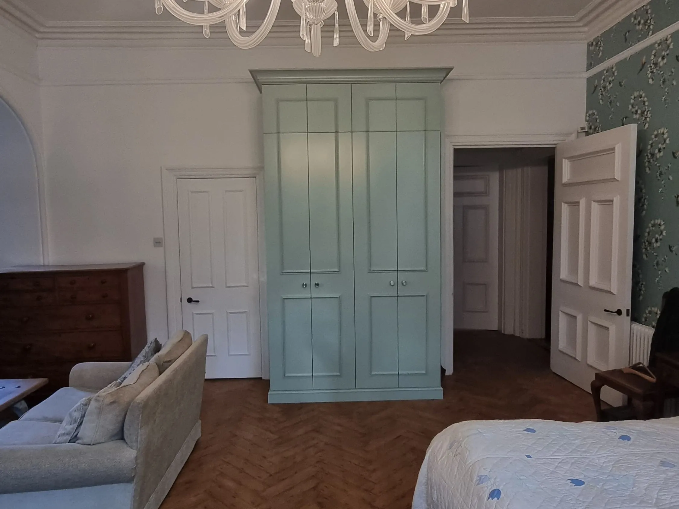 Painted green fitted wardrobe in a period bedroom with herringbone floor