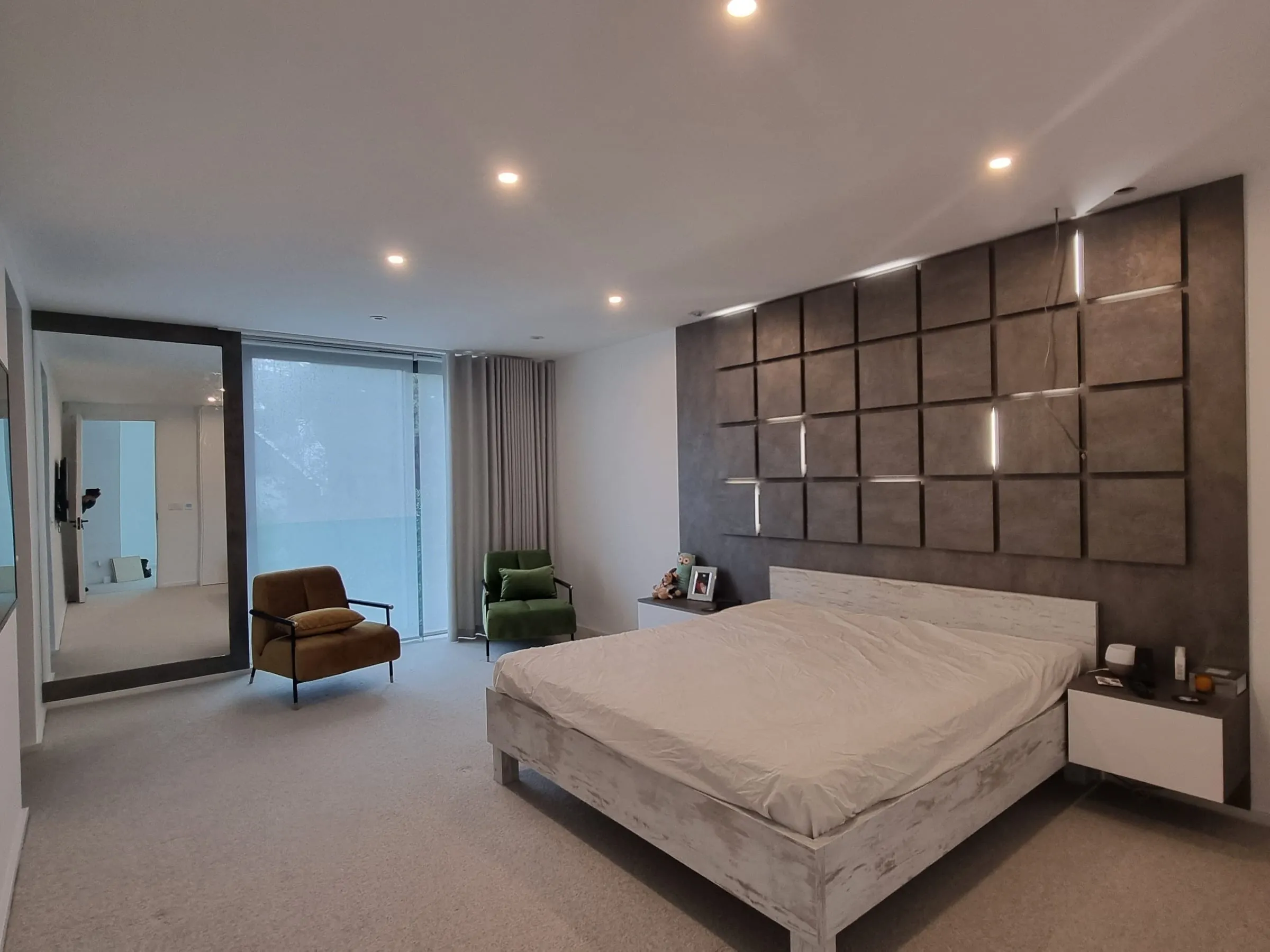 Bedroom with white handleless wardrobes and a padded panel headboard wall