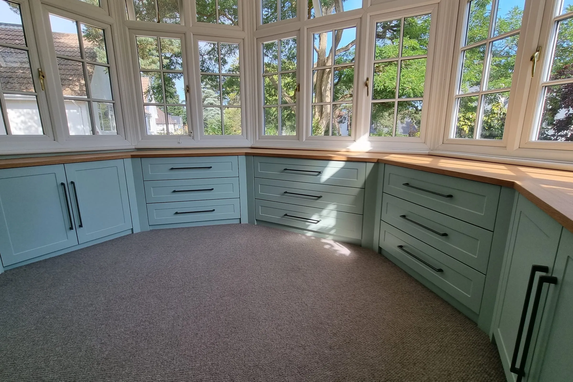 Painted fitted drawer units with an oak worktop running around a bay window