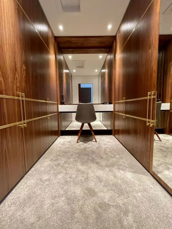Walk-in wardrobe with walnut-veneered doors, brass handles and a dressing table at the far end