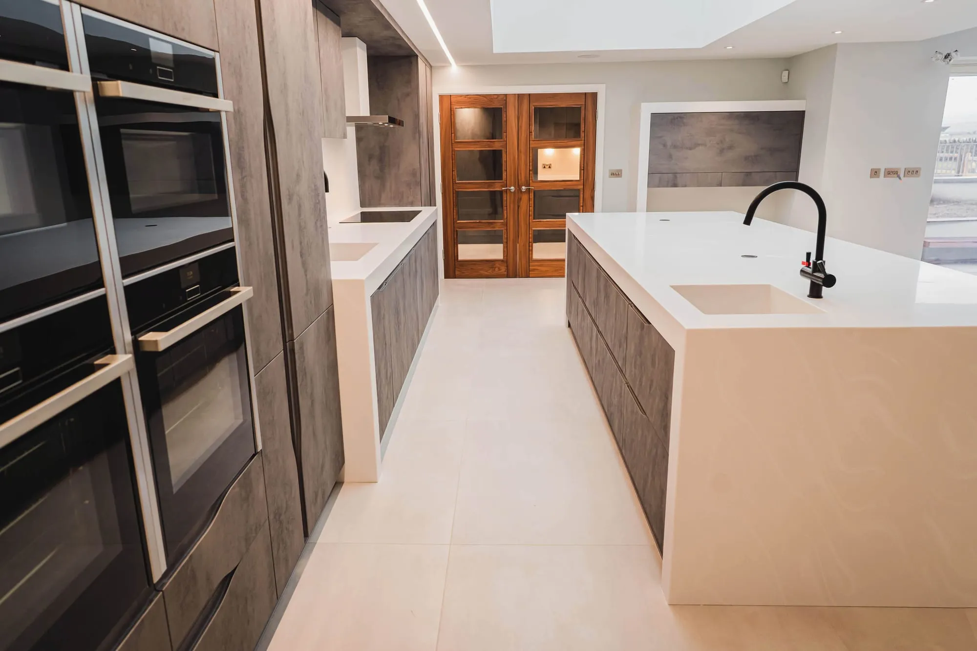 Kitchen aisle with integrated ovens in tall concrete-effect units