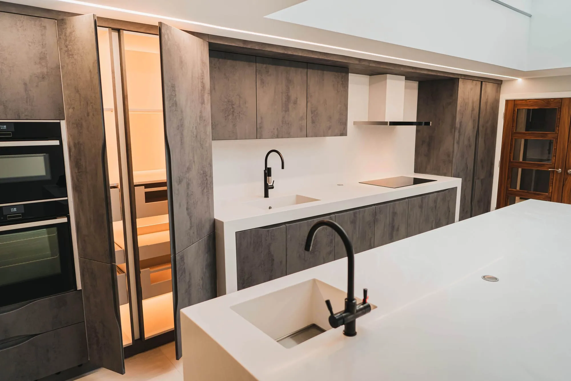 Open pantry cupboard beside the sink in a concrete-effect kitchen