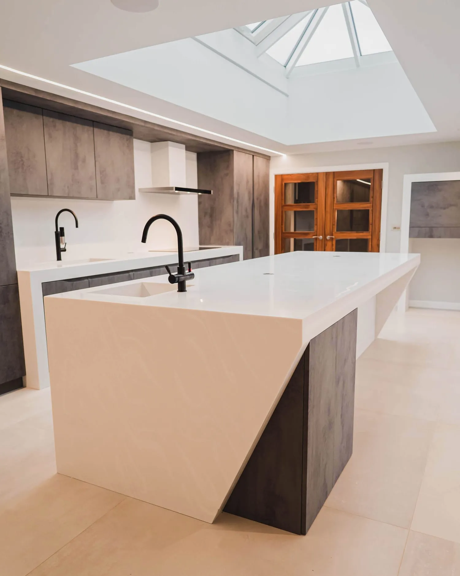 White angular kitchen island under a rooflight, seen from the end