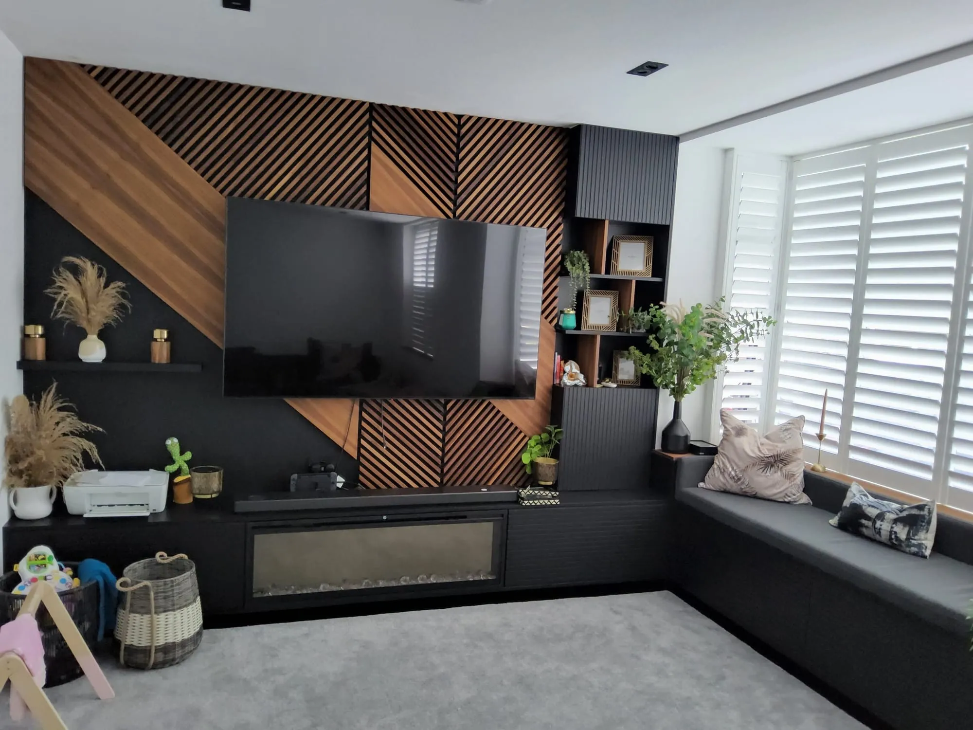 Media wall with diagonal walnut slats, a wall-mounted TV, an inset fire and a built-in window seat