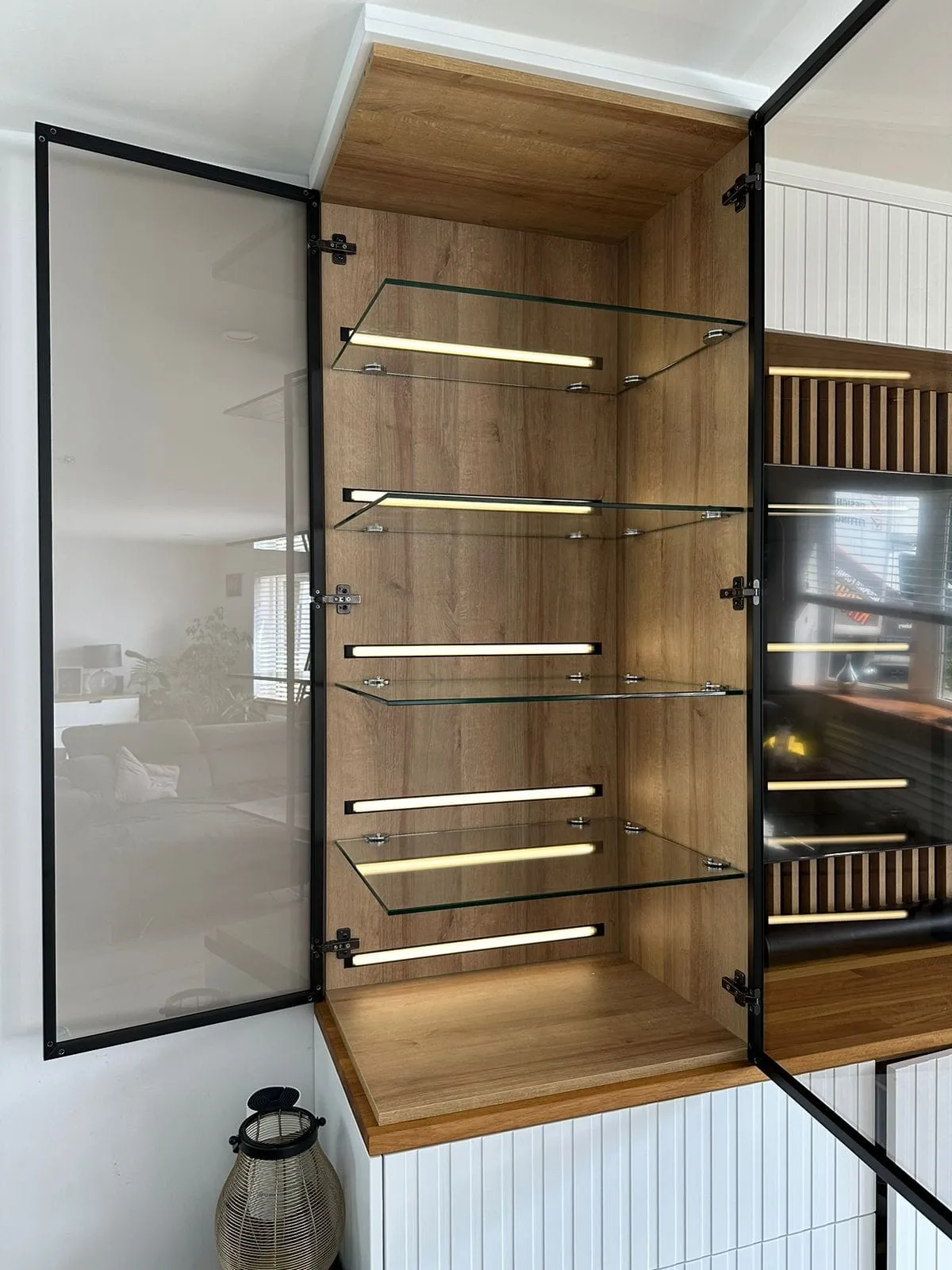 Open glass display cabinet with lit shelves in an oak media wall
