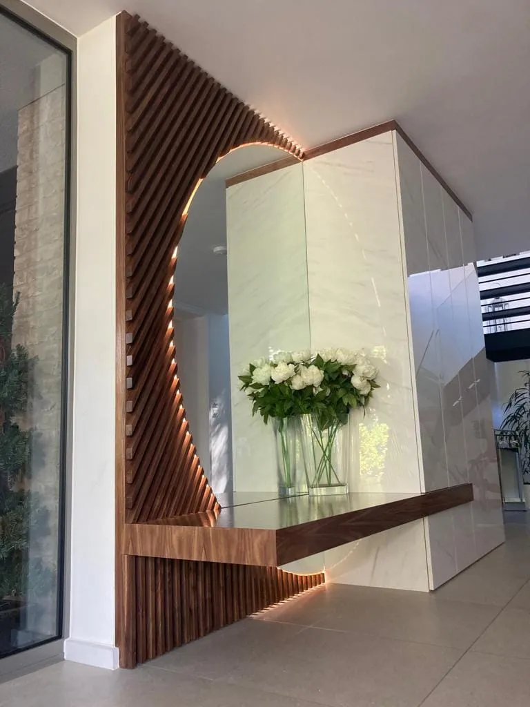 Walnut slatted feature wall with a curved lit mirror and a floating walnut shelf in a hallway