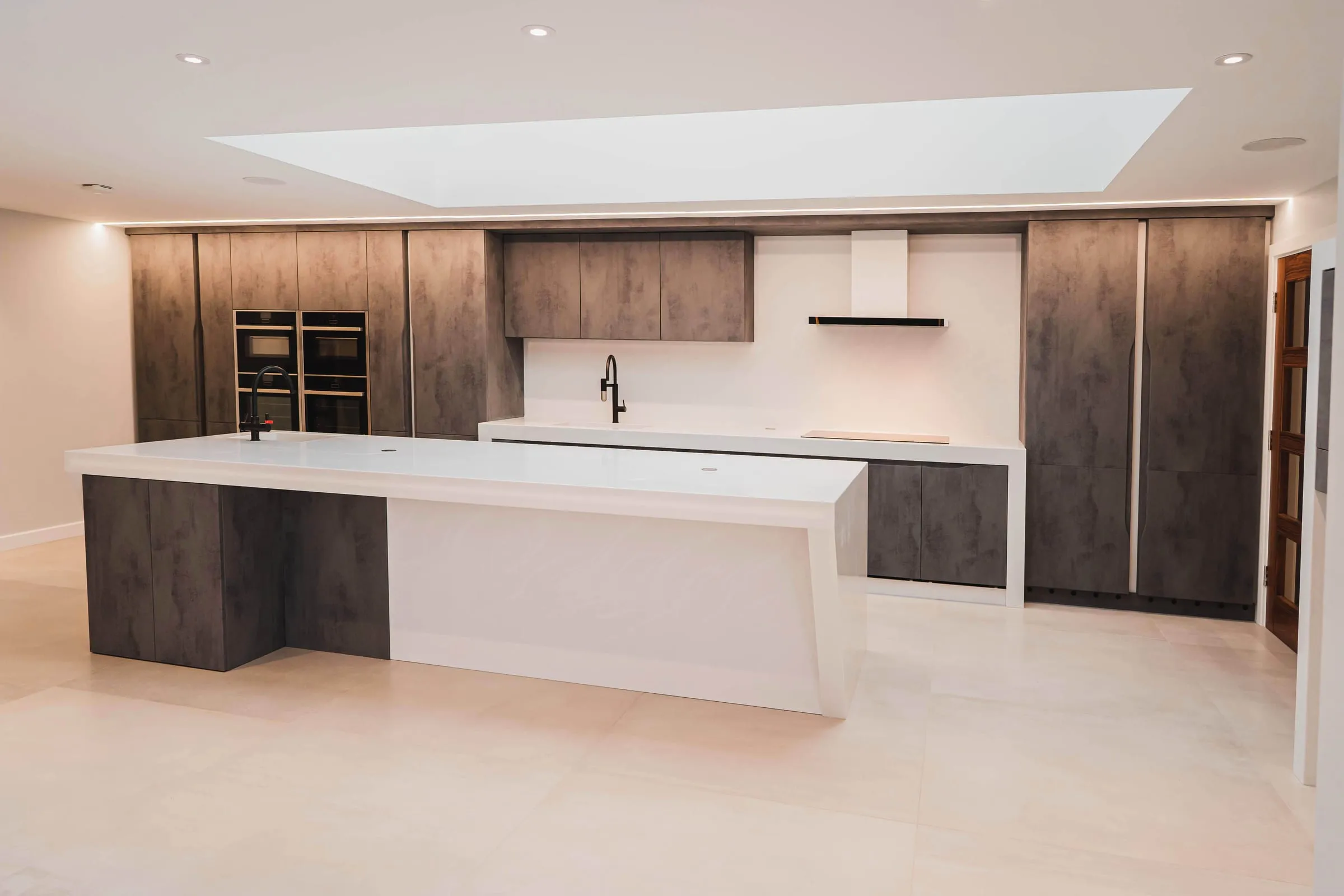 Fitted kitchen with a white island and concrete-effect cabinets under a rooflight