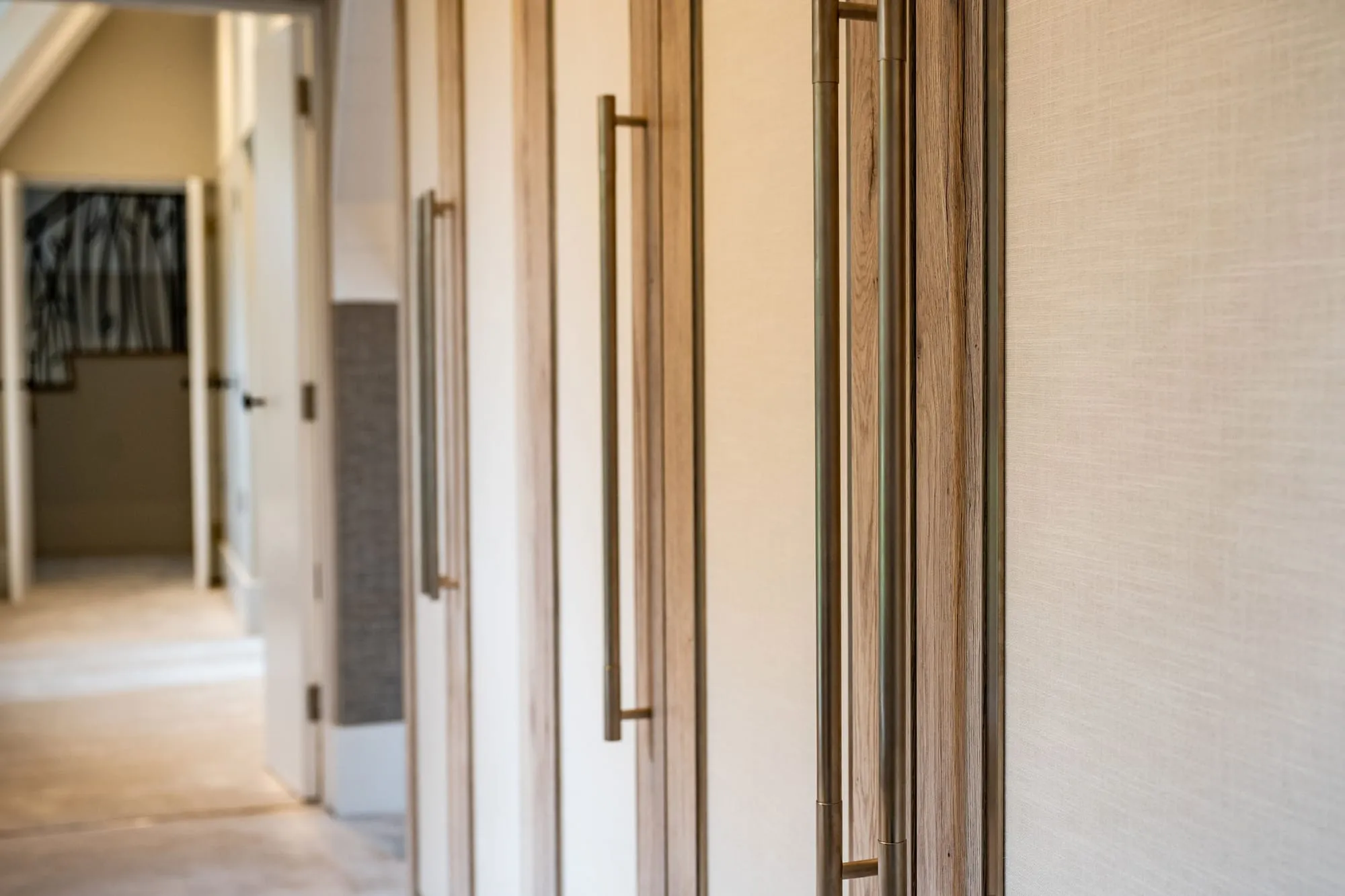 Full-height fitted wardrobes with oak and linen-effect doors and long brass handles along a landing